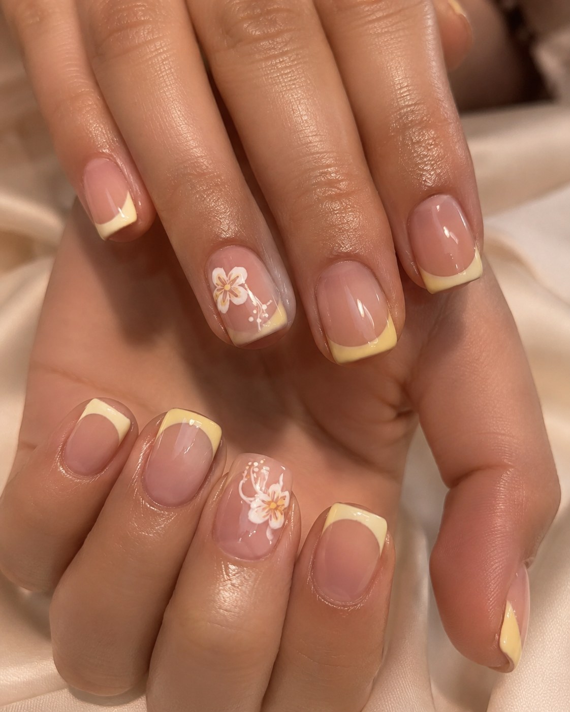 Short summer nails featuring soft yellow French tips and a hand-painted flower design